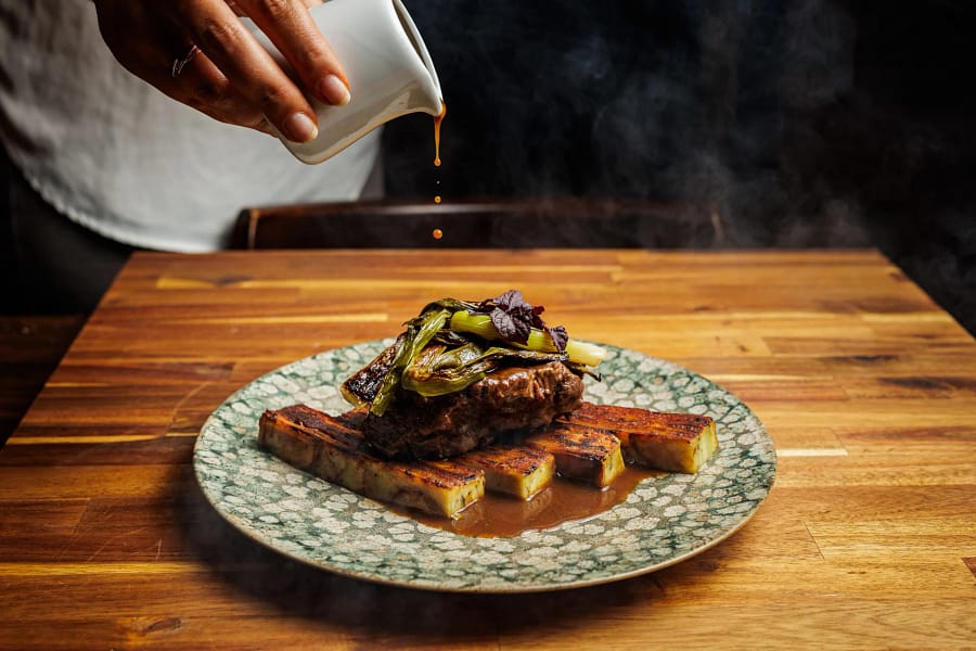 Chef assaisonnant un plat de viande – La Belle Quille Chef de La Belle Quille assaisonnant un plat de viande avec du jus