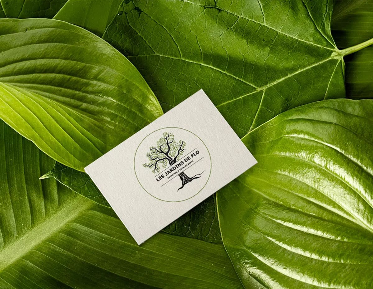 Carte de visite texturée posée sur des feuilles vertes tropicales, présentant le logo Les Jardins de Flo.